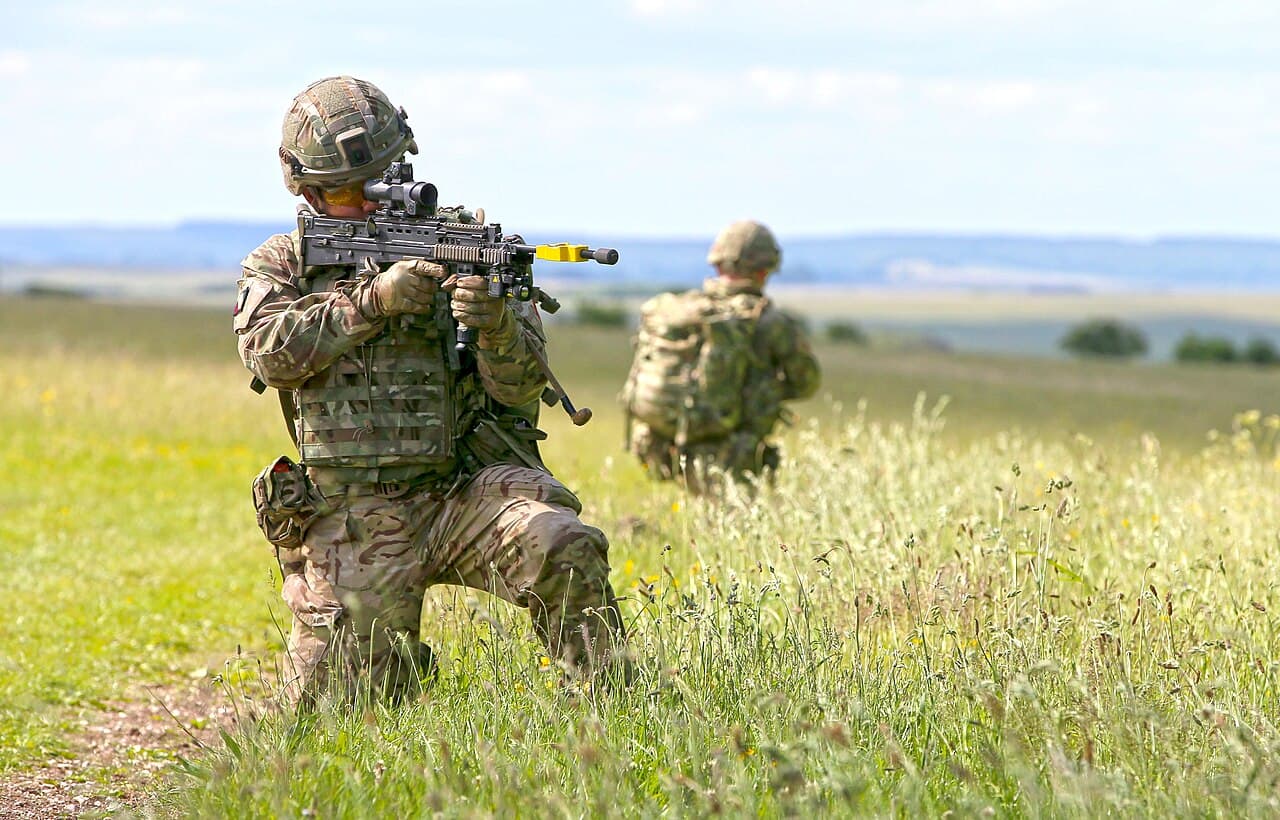 Soldier kneeling in the field wearing a plate carrier and load-carrying system
