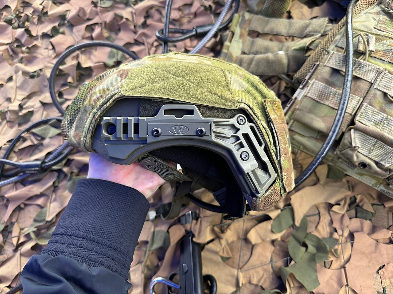 High-cut ballistic helmet with accessory rails, held over a plate carrier