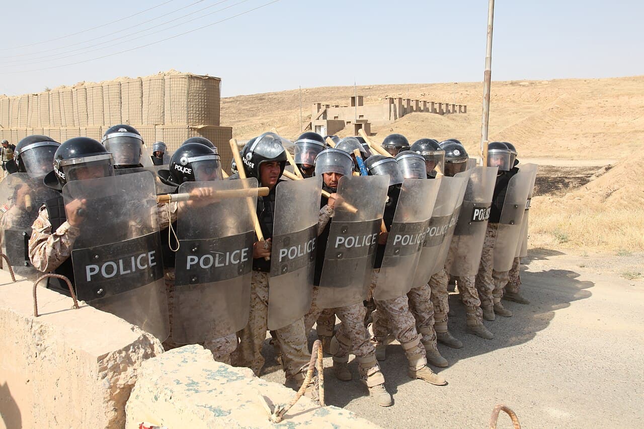 Police unit in a riot control formation behind body shields, with helmets and batons